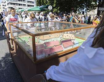 Festzug: Modell in Glaskasten wird gezogen