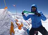 Mann hebt Fahne auf verschneitem Gipfel in Kamera