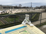 Seehas-Kuscheltier sitzt auf Plan vor Märzfeld und Eiffelturm in Paris