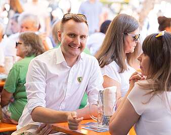 Menschen an Biertischen, junger Mann schaut in Kamera