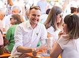 Menschen an Biertischen, junger Mann schaut in Kamera