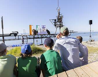 Menschen verfolgen ökumenischen Freiluftgottesdienst mit Altar auf Klangschiff