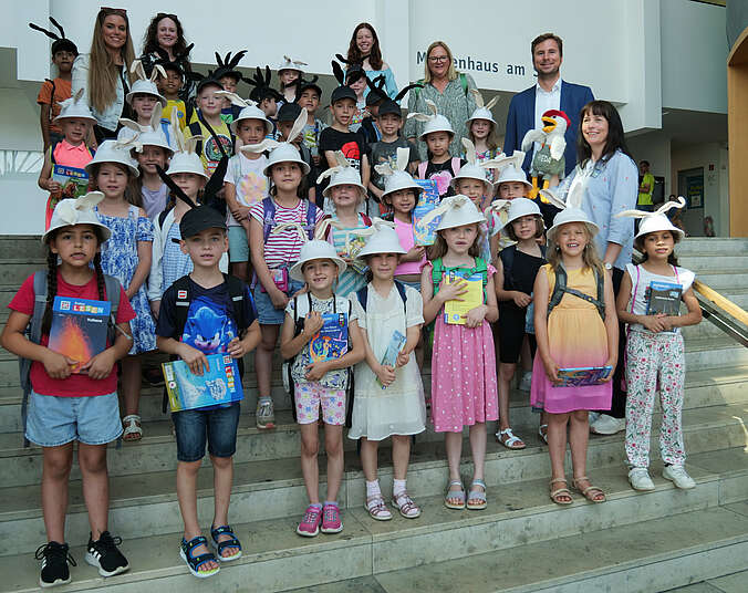Mädchen und Jungen mit schwarzen Hasenohren stehen auf der Treppe. In den Händen halten sie jeweils ein Buch.