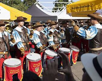 Fanfarenzug spielt und trommelt zwischen Sonnenschirmen