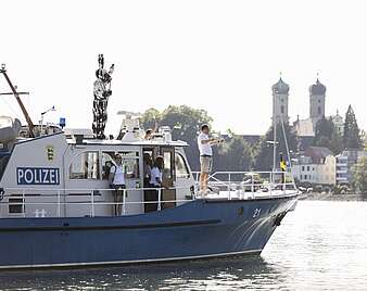 Mann in Hasenkostüm steht auf Polizeiboot und Wink, im Hintergrund Schlosskirche