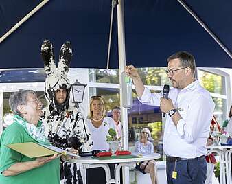 Ehrung von Frau von Mann in Hasenkostüm, weiterer Mann spricht in Mikrofon