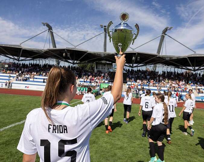 Frau im Fußballtrikot zeigt Pokal